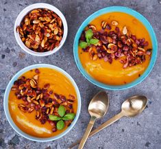 three bowls filled with food next to spoons on top of a cement surface,