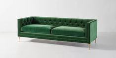 a green velvet couch with gold legs and buttons on the back, sitting against a white wall