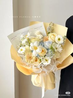 a woman holding a bouquet of white and yellow flowers in her hand with an envelope