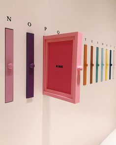 there is a pink box hanging on the wall next to other colored doors and letters