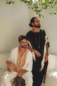 two men sitting next to each other in front of a tree