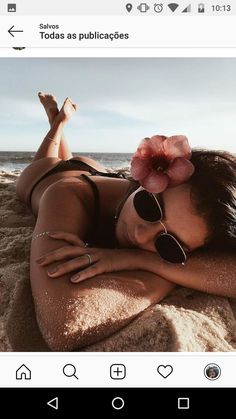 a woman laying on top of a sandy beach next to the ocean wearing sunglasses and a flower in her hair