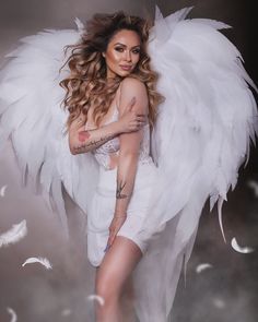 a woman with white wings on her body and chest posing for a photo in front of feathers