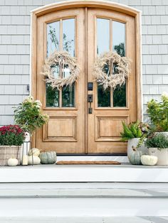 two wreaths on the front door of a house with potted plants next to it