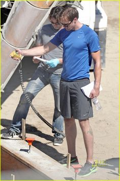 a man in blue shirt and black shorts holding a hose next to another man on a boat