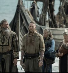 a group of people standing next to each other on a beach near an old ship