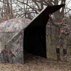 a man standing next to a tent in the woods