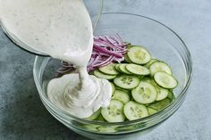 cucumbers and onions are being mixed in a bowl with ranch dressing on the side