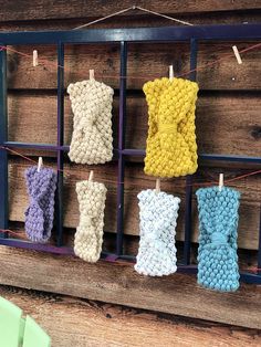 knitted items hanging on clothes pins in a display case against a wooden wall with pegs