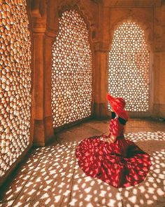 a woman in a red dress is sitting on the floor with her shadow cast onto the wall