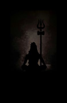 the silhouette of a person sitting in front of a pole with a demon on it