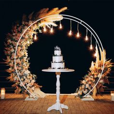 a cake sitting on top of a white table under a circular arch with candles and flowers