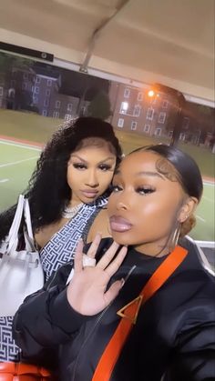 two women standing next to each other in front of a tennis court with one holding her hand up