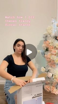 a woman sitting on the floor opening a box with flowers behind her and text reading watch how i diy these trendy floral stands