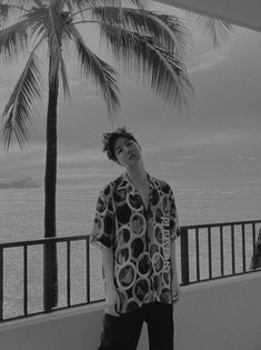 a man standing next to a palm tree on top of a balcony near the ocean