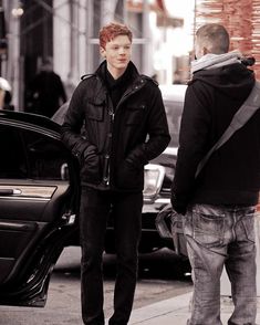 two young men standing on the sidewalk talking to each other