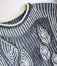 a close up of a knitted sweater on a hanger next to a white wall