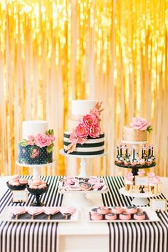 a table topped with cakes and cupcakes next to a gold foil curtain covered wall