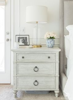 a white dresser with two drawers and a lamp