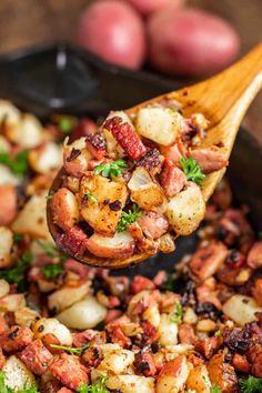 a wooden spoon full of potatoes and meat with parsley on the side, in a skillet