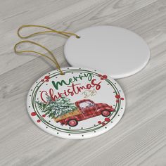 a christmas ornament with a red truck and pine tree on it sitting on a wooden surface