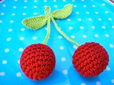 two crocheted strawberries on a blue plate with white dots and a green leaf