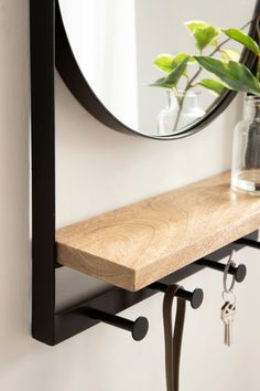 a mirror hanging on the wall next to a shelf with a vase and key holder