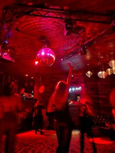 people dancing in a club at night with red lights and disco balls hanging from the ceiling