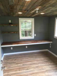 empty room with wood flooring and built - in shelves on the far wall, looking out onto trees