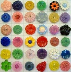 many different colored buttons are arranged on a white surface with squares in the middle and flowers at the bottom