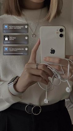 a woman holding an iphone in front of her face with ear buds attached to it