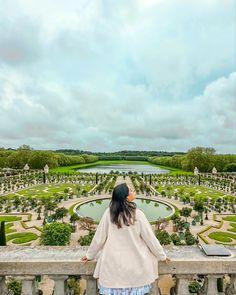 a woman standing on top of a balcony next to a lush green park