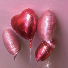 three shiny heart shaped balloons on a pink background