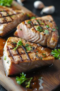 two pieces of fish sitting on top of a wooden cutting board next to garlic and parsley