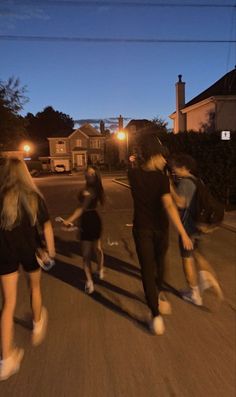 three people are skateboarding down the street at night, with one person walking behind them