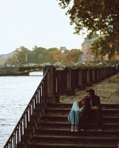 two people are sitting on some steps by the water