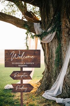 a wooden sign sitting under a tree in the grass