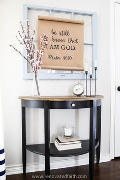 a small table with a sign on the wall above it and a vase filled with flowers