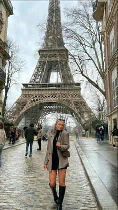 a woman standing in front of the eiffel tower with her legs crossed and holding an umbrella