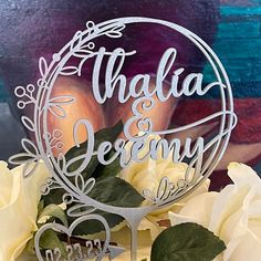 a wedding cake topper with the words thaala and jenny on it, surrounded by white roses