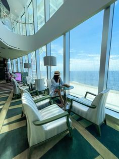 a man sitting in a chair next to a window looking out at the ocean on top of a tall building