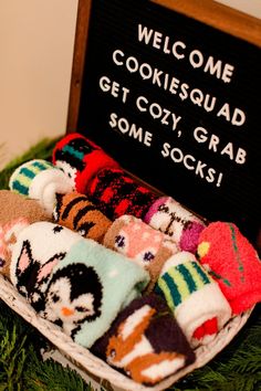 a basket filled with socks sitting on top of a green table next to a sign that says welcome cookiesquaad get cozy grab some socks