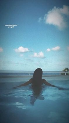 a woman is sitting in the water with her back to the camera and looking at the sky