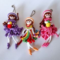 three small knitted dolls hanging from strings on a white surface, one wearing a hat and the other in a dress