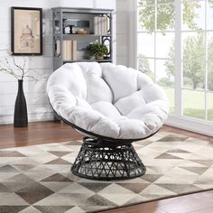 a white chair sitting on top of a wooden floor next to a book shelf and window