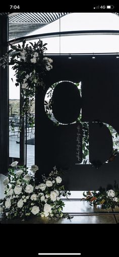 the letter d is surrounded by flowers and greenery in front of a large window