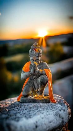 a buddha statue sitting on top of a stone wall with the sun setting in the background