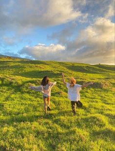 two girls running in the grass with their arms outstretched