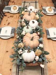 a wooden table topped with lots of white pumpkins and greenery on top of it