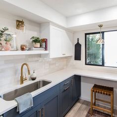 a kitchen with blue cabinets and white counter tops, gold faucets and a wooden stool